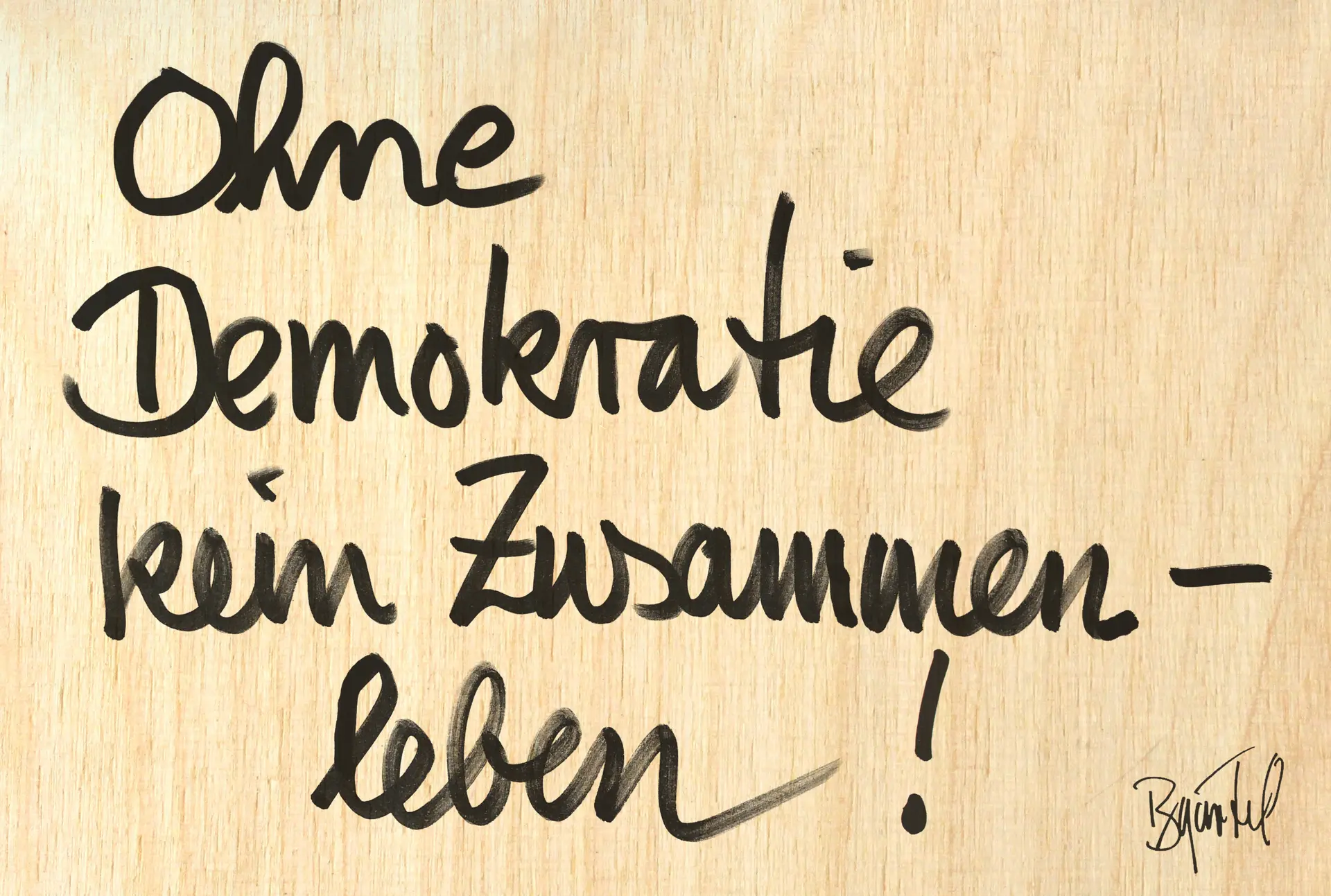 Auf einem Holztisch steht mit Edding "Ohne Demokratie kein Zusammenleben".