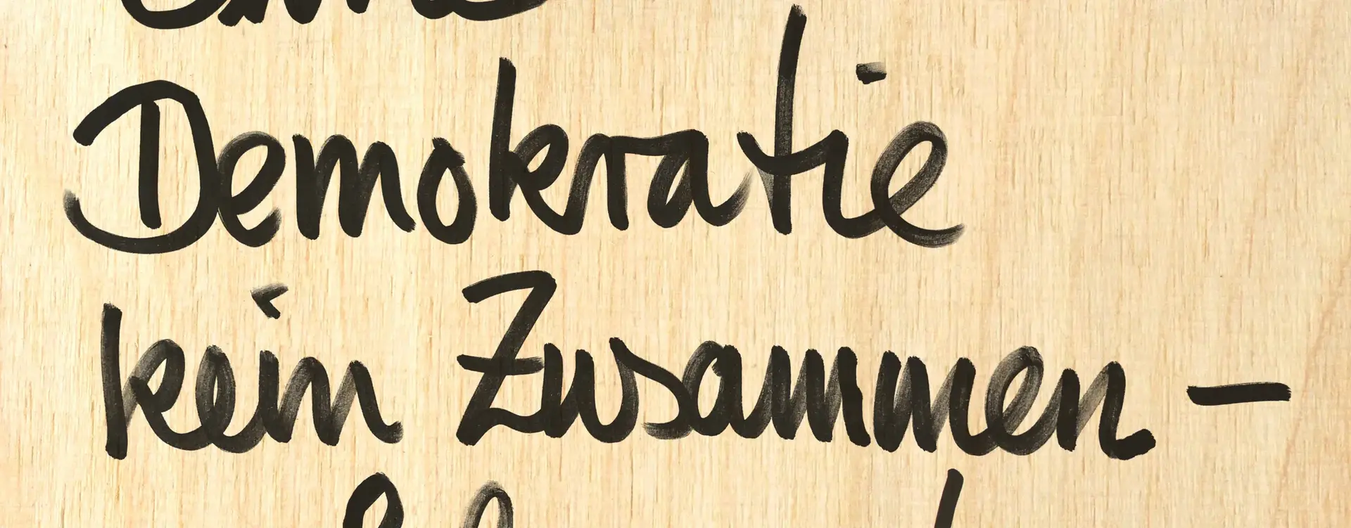 Auf dem Bild sieht man mit Edding auf einen Holztisch "Ohne Demokratie kein Zusammenleben" geschrieben.