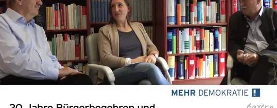 Auf dem Bild sitzen zwei ältere Männer und eine Frau. Unter dem Bild steht "20 Jahre Bürgerbegehren und Bürgerentscheide in Bayern."