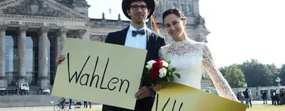 Die Braut und der Bräutigam stehen nun mit den Plakaten vor dem Bundestag auf der Wiese.
