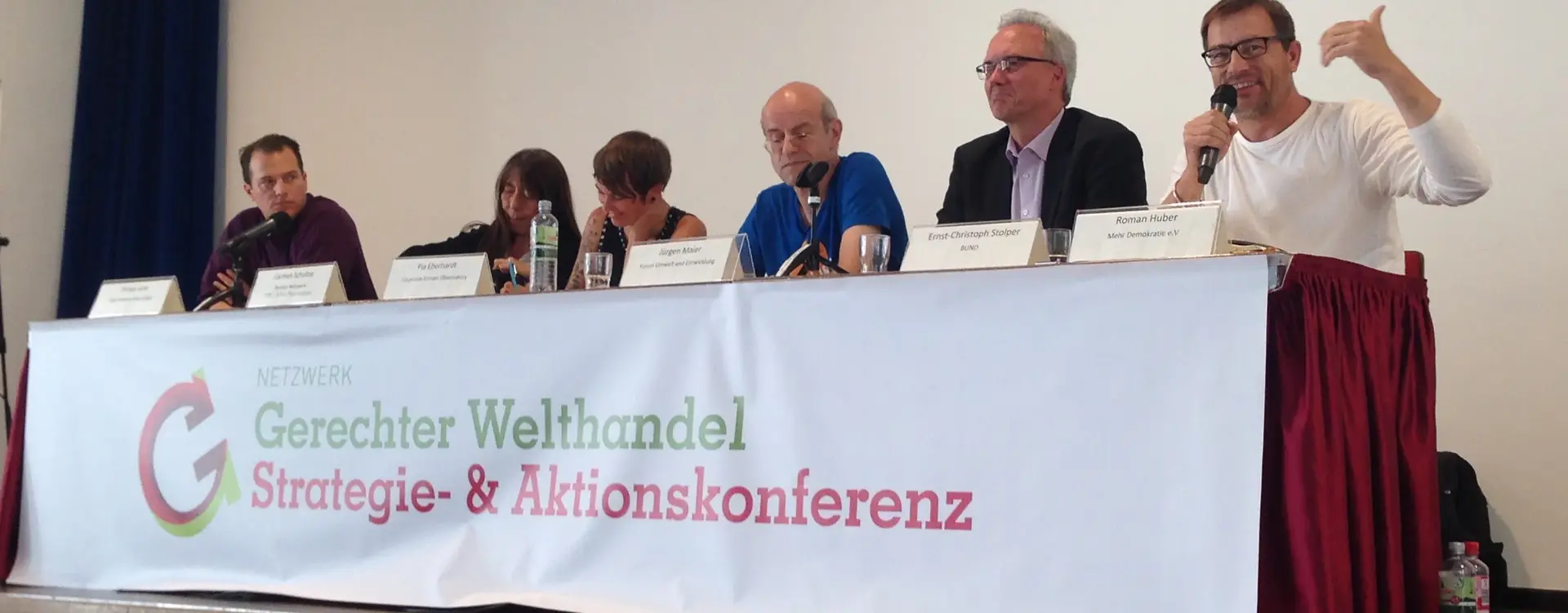 Sechs Personen sitzen auf einer Bühne vor einem Tisch, mit dem Transparent "Gerechter Welthandel, Absatz Strategie- & Aktionskonferenz".