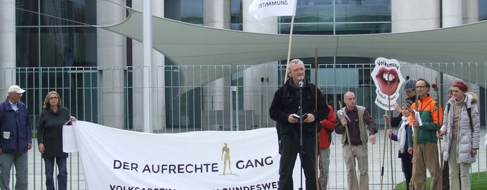 (Michael von der Lohe hält eine Rede vor dem Bundeskanzleramt) Vor dem Kanzleramt hält ein Mann auf Palletten eine Rede.