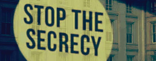 Auf dem Bild wird ein Gebäude angestrahlt, mit den Worten "STOP THE SECRECY".