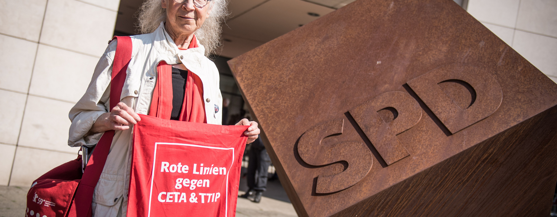 Vor dem Willy-Brandt-Haus steht eine ältere Dame, mit einem roten Tuch und der Aufschrift "Rote Linien gegen CETA & TTIP".