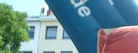 Auf dem Bild ist ein circa vier mal fünf Meter großes, aus Plastik aufgeblasenes Rechteck, mit der Aufschrift "Kommunale-verfassung", von oben steckt ein Pfeil aus Plastik darin, mit der Aufschrift "Faire Volksentscheide".
