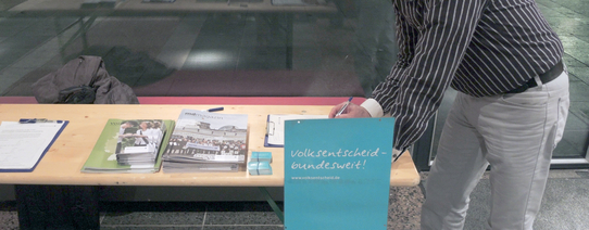 Ein Mann unterschreibt gerade an einem Stand von Mehr Demokratie.