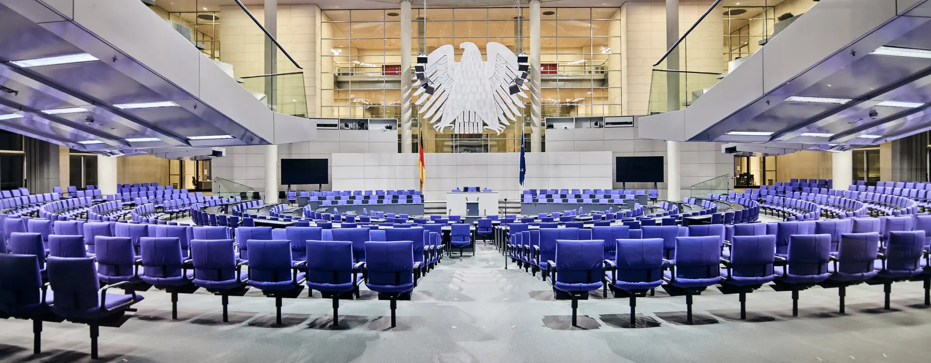 Auf dem Bild ist ein leerer Bundestag und im Zentrum ist der Bundesadler.