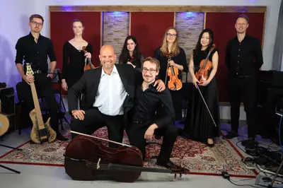 Zu sehen sind sechs Menschen mit Musikinstrumenten, welche alle in die Kamera gucken.