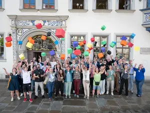 Viele Menschen stehen vor einem Gebäude und lassen Luftballons steigen.