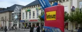 Ein circa vier mal fünf Meter großes aufgeblasenes Rechteck, steht auf einem Marktplatz, mit der Aufschrift "Verfassung" und einem Pfeil darin, mit der Aufschrift "FAIRE VOLKSENTSCHEIDE".