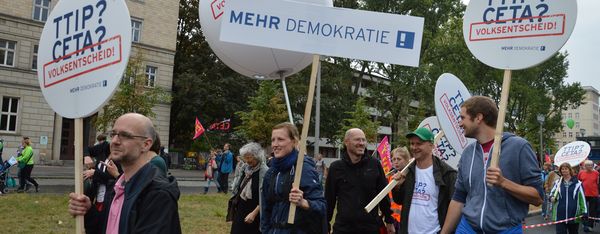 Menschen laufen mit der Aufschrift "TTIP? CETA? Volksentscheid" auf Schilder herum.