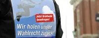 Ein Mensch hat ein Plakat auf dem Rücken, mit der Aufschrift "Wir holen unser Wahlrecht zurück!".