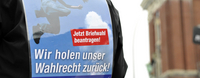 Ein Mensch hat ein Plakat auf dem Rücken, mit der Aufschrift "Wir holen unser Wahlrecht zurück!".
