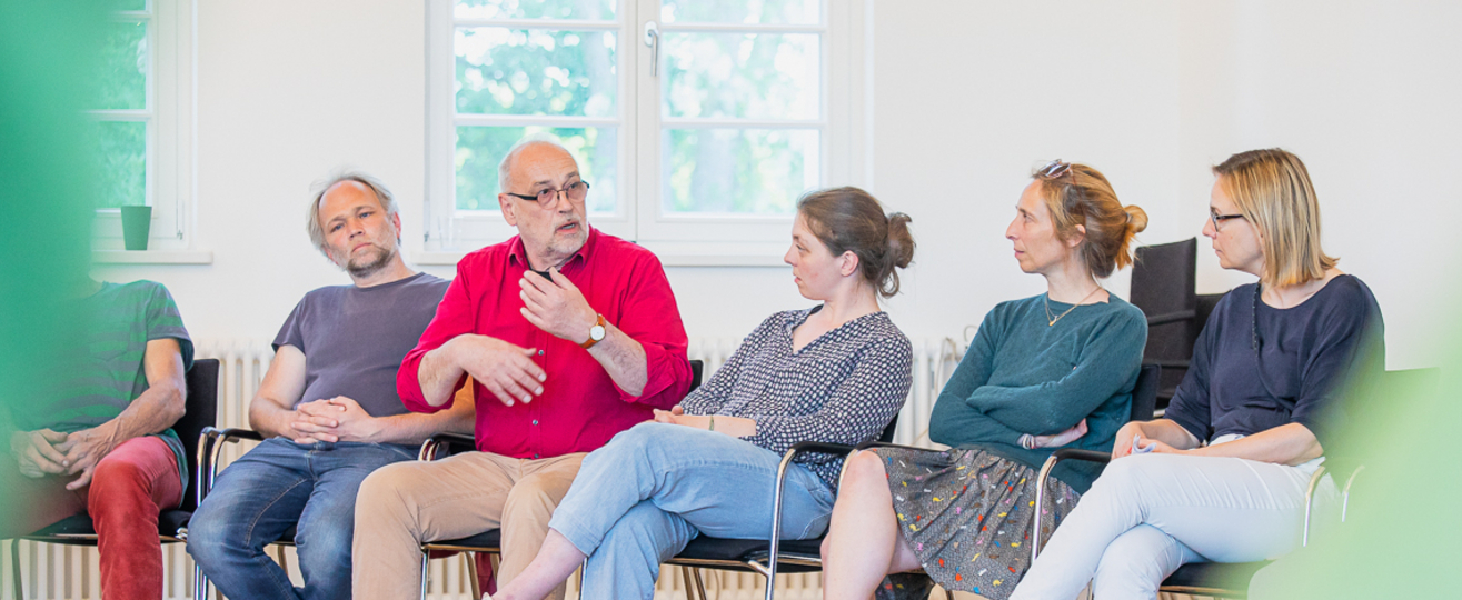 5 Menschen sitzen nebeneinander, einer spricht.