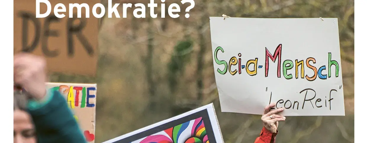 Zu sehen ist das Deckblatt von der Magazin Ausgabe vom 01.2024. Zu sehen ist ein Protestmarsch, wo ein Mann ins Auge fällt, der der Schild hochhält mit den Worten: Sei-d-Mensch ´Leon Reif´. Links-oben im Vordergrund steht: Was stärkt die, Absatz Demokratie.
