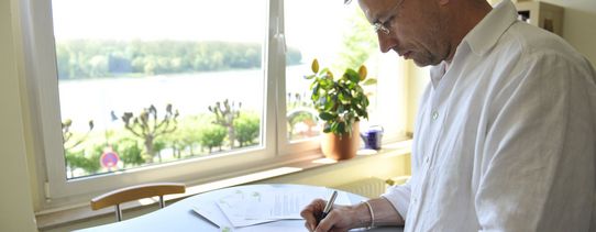 Ein Bild von Roman Huber (Er ist Geschäftsführender Bundesvorstand), unterschriebt auf einem Stehtisch Blätter auf dem Bild.