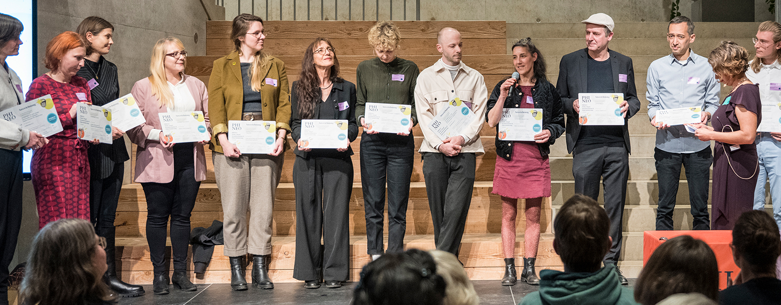 Menschen auf einer Bühne. Sie halten eine Auszeichnung in den Händen
