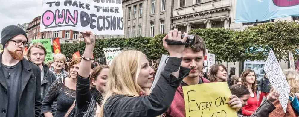 Auf dem Bild ist ein Protest zu sehen und im Fokus steht ein junge Frau mit dem Plakat "I TRUST WOMEN TO MAKE THEIR OWN DECISIONS".