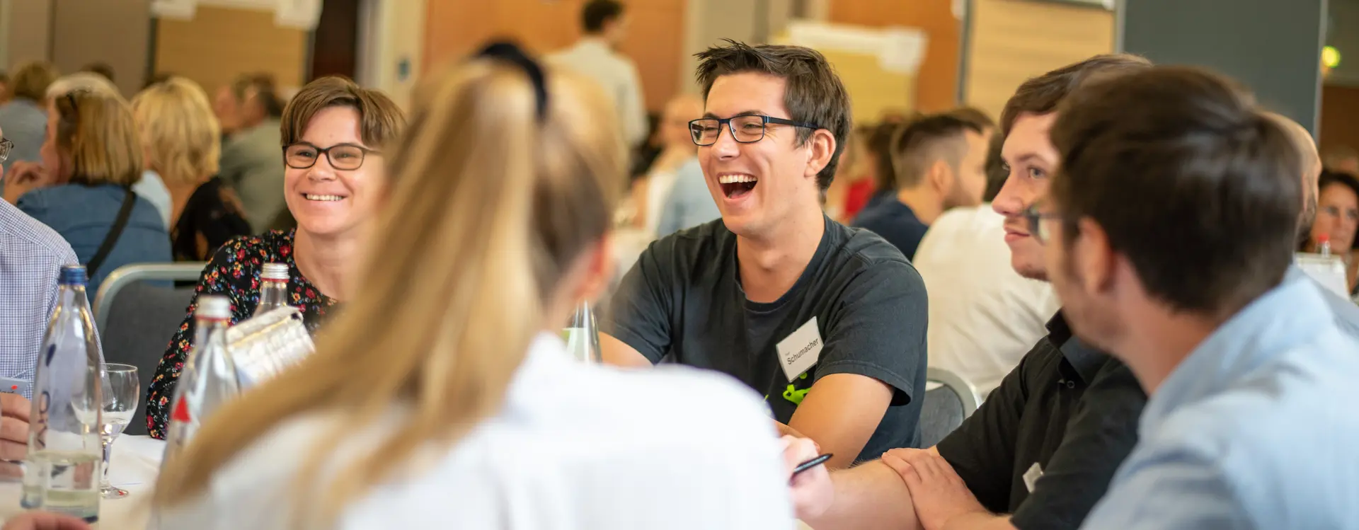 Viele Menschen, die zusammensitzen, teils lachen und den Anschein haben, zu diskutieren. 