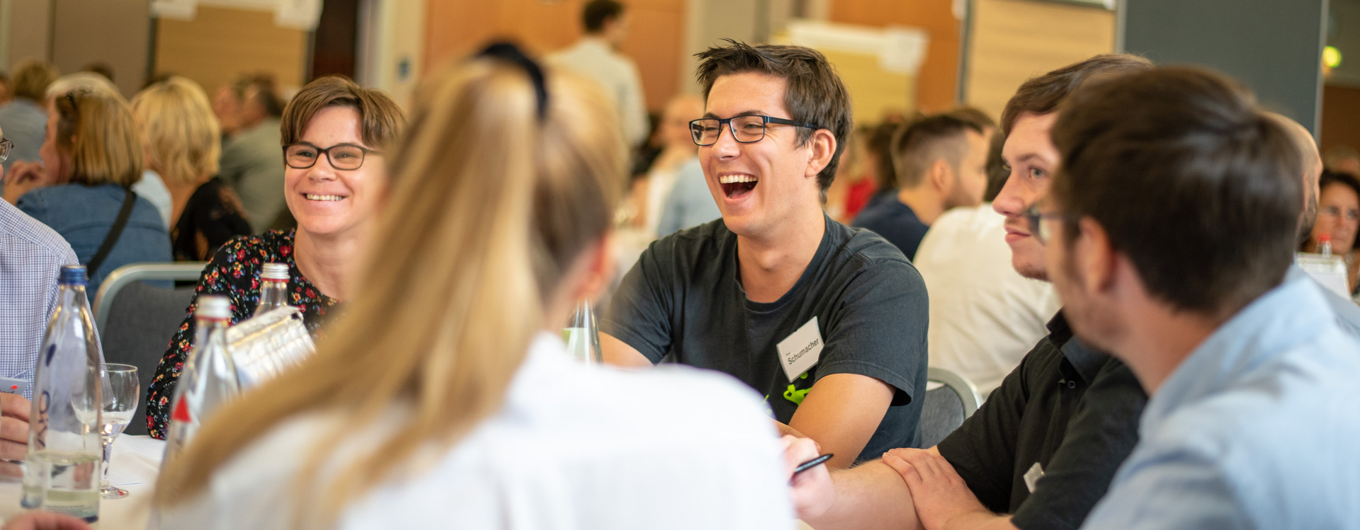 Viele Menschen, die zusammensitzen, teils lachen und den Anschein haben, zu diskutieren.