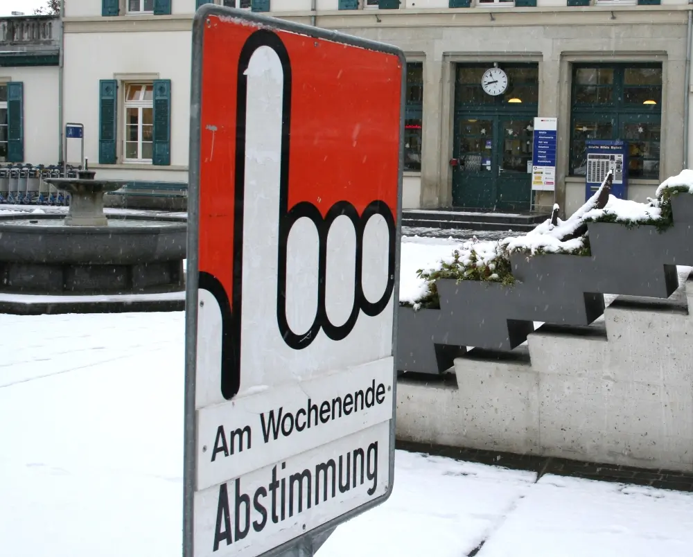 Auf einem Plakataufsteller ist eine Hand mit erhobenem Zeigefinger zu sehen, wo unten "Am Wochenende Abstimmung" steht.