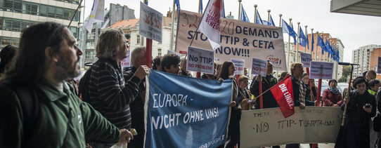 ("Stop TTIP"-Aktion gegen TTIP und CETA vor dem Gebäude der EU-Kommission in Brüssel. | Foto by Alexander Garrido Delgado | Lizenz: CC BY-SA 2.0) Vor dem Gebäude der EU-Kommission stehen Demonstranten.