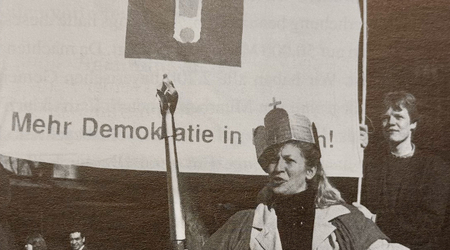 Aktion Der Bürger wird König/Die Bürgerin wird Königin während des Volkksbegeherens Mehr Demokratie in Bayern 1995. Man sieht eine zur Königin gekrönte Bürgerin mit einem Szepter, auf einem Thron sitzend. Im Hintergrund ein Plakat mit der Aufschrift Mehr Demokratie in Bayern und dem Logo mit dem Ausrufezeichen.