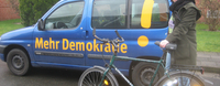 Ramona Pump ist mit einem Fahrrad vor dem Mehr Demokratie Auto.