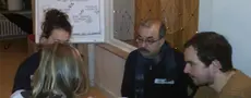 Auf dem Bild sitzen vier Personen an einem kleinen Tisch zusammen und reden.