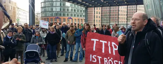 (Bundesvorstandssprecher Dr. Michael Efler hält auf dem Potsdamer Platz in Berlin eine emotionale Rede gegen TTIP und CETA | Foto by Charlie Rutz | Lizenz: CC BY-SA 2.0) Zu sehen ist ein Protestmarsch.
