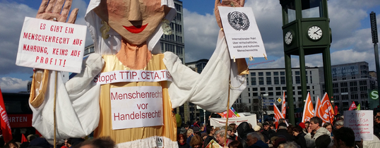 Eine übergroße Puppe hat Plakate auf sich, welche den Stopp von TTIP, CETA & TiSA fordern. Auf ihrem Kopf als Krone steht "HUMANRIGHT".