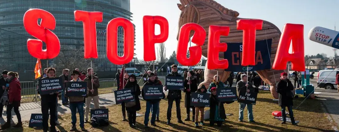 Auf dem Bild sind circa 20 Menschen, manche von ihnen halten rote aufgeblasene Luftballons hoch, welche "STOP CETA" ergeben.