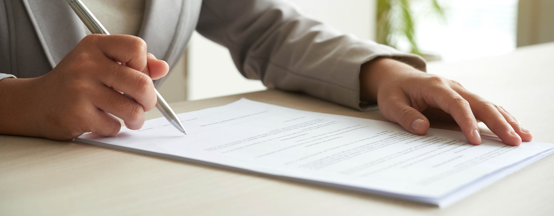 Auf dem Bild sieht man eine Frau mit einem Stift ein Blatt Papier unterschreiben.