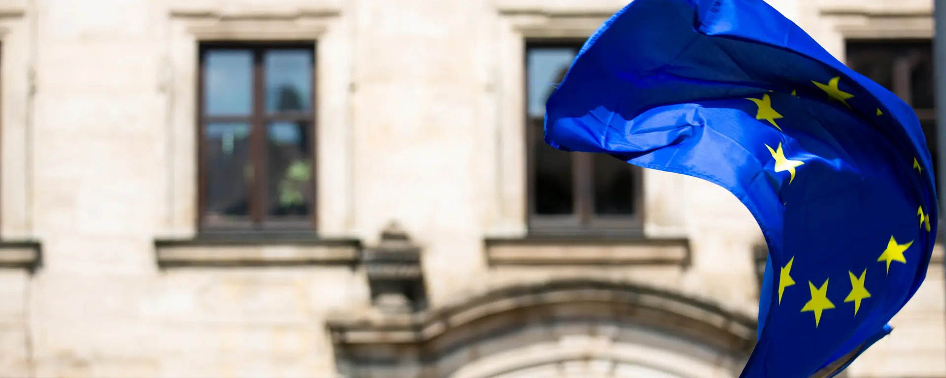 Auf dem Bild ist eine verwehte Europaflagge vor einem Gebäude zu sehen.