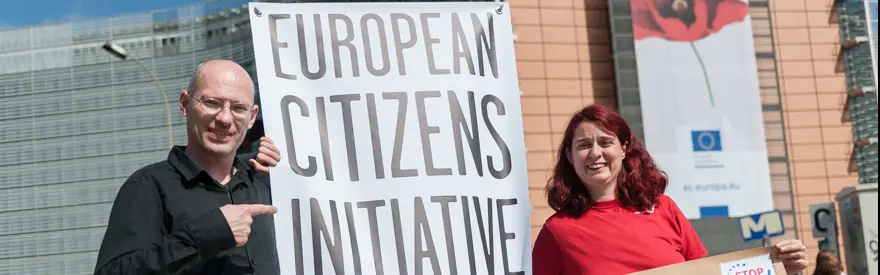 Auf dem Bild sind zwei Personen im Fokus, mit der Aufschrift "European Citizens Initiative" auf einem Transparent.