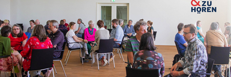 Foto einer Sprechen-und-Zuhören-Veranstaltung mit Menschen auf Stühlen in Gruppen sitzend