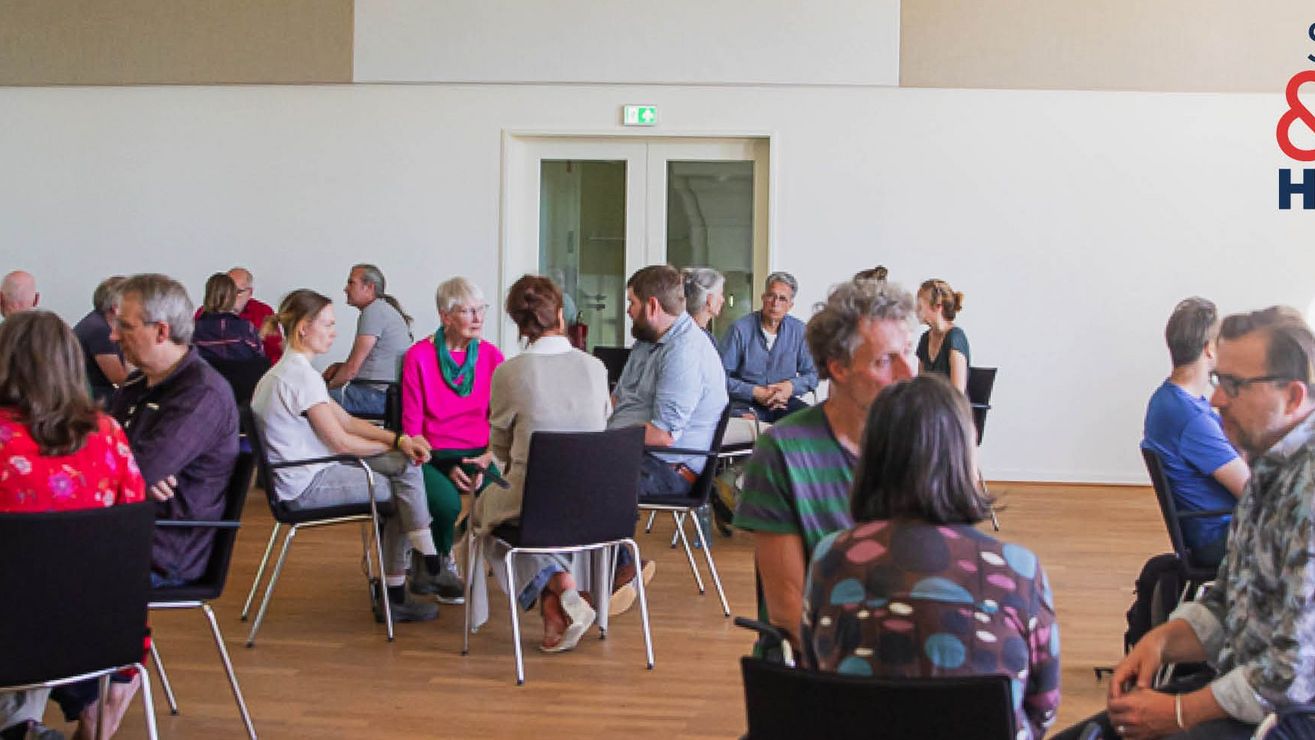 Foto einer Sprechen-und-Zuhören-Veranstaltung mit Menschen auf Stühlen in Gruppen sitzend