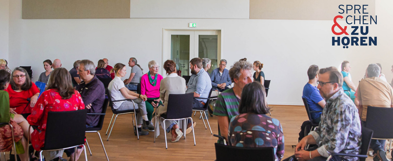 Foto einer Sprechen-und-Zuhören-Veranstaltung mit Menschen auf Stühlen in Gruppen sitzend