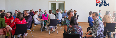 Foto einer Sprechen-und-Zuhören-Veranstaltung mit Menschen auf Stühlen in Gruppen sitzend