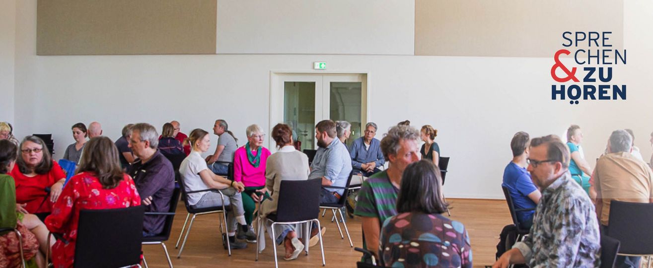 Foto einer Sprechen-und-Zuhören-Veranstaltung mit Menschen auf Stühlen in Gruppen sitzend