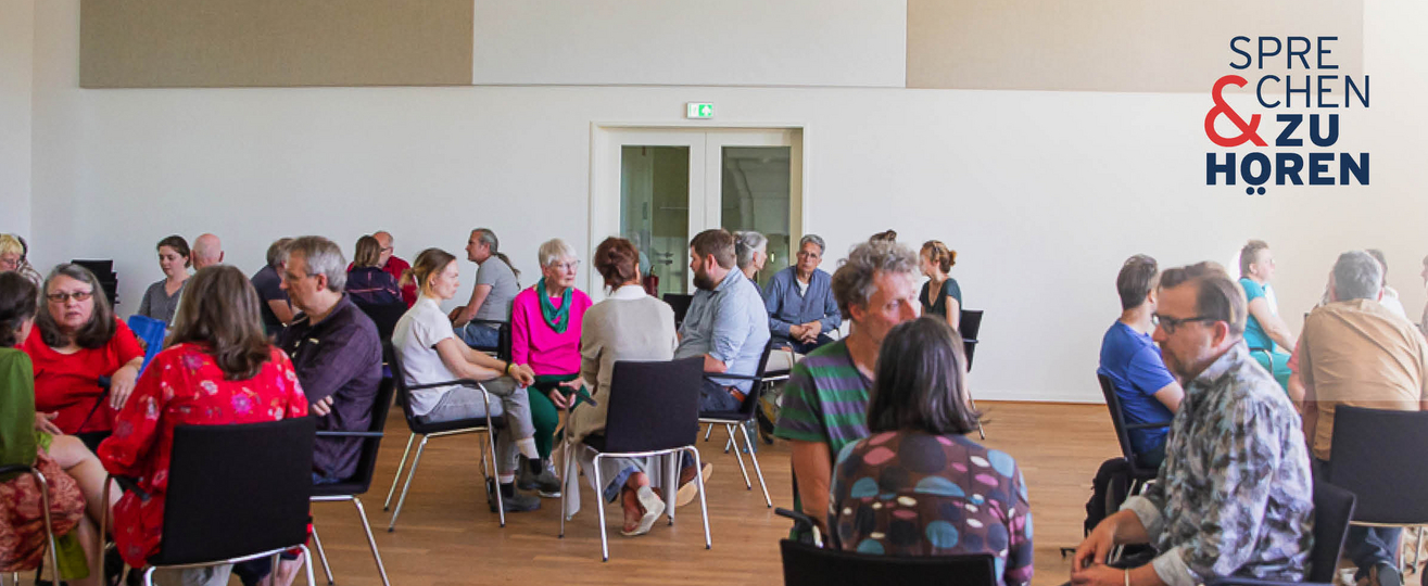 Foto einer Sprechen-und-Zuhören-Veranstaltung mit Menschen auf Stühlen in Gruppen sitzend