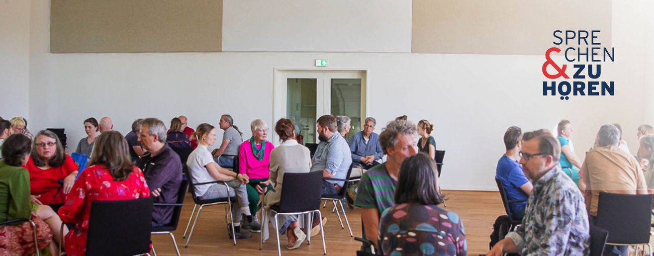 Menschen in Stuhlkreisen (3-4 Personen) in einem hellen Saal, oben rechts das Logo „Sprechen & Zuhören".
