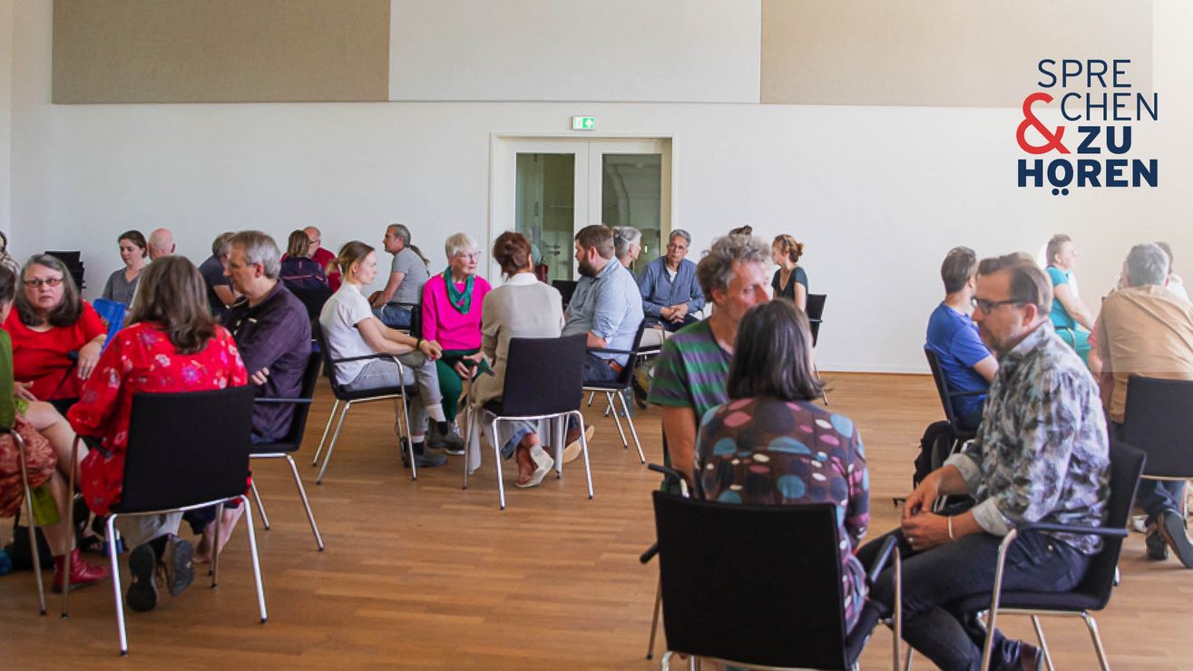 Foto einer Sprechen-und-Zuhören-Veranstaltung mit Menschen auf Stühlen in Gruppen sitzend