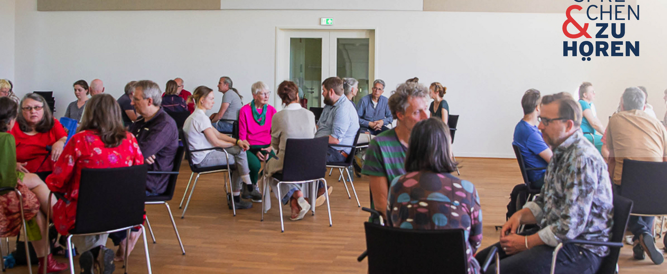 Foto einer Sprechen-und-Zuhören-Veranstaltung mit Menschen auf Stühlen in Gruppen sitzend