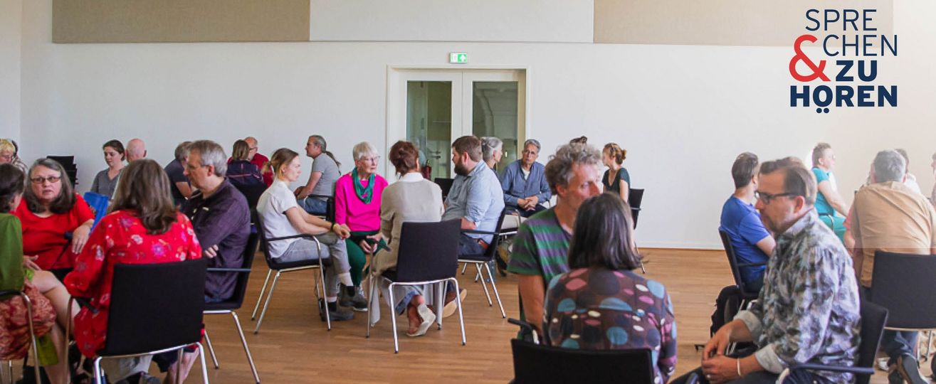 Foto einer Sprechen-und-Zuhören-Veranstaltung mit Menschen auf Stühlen in Gruppen sitzend