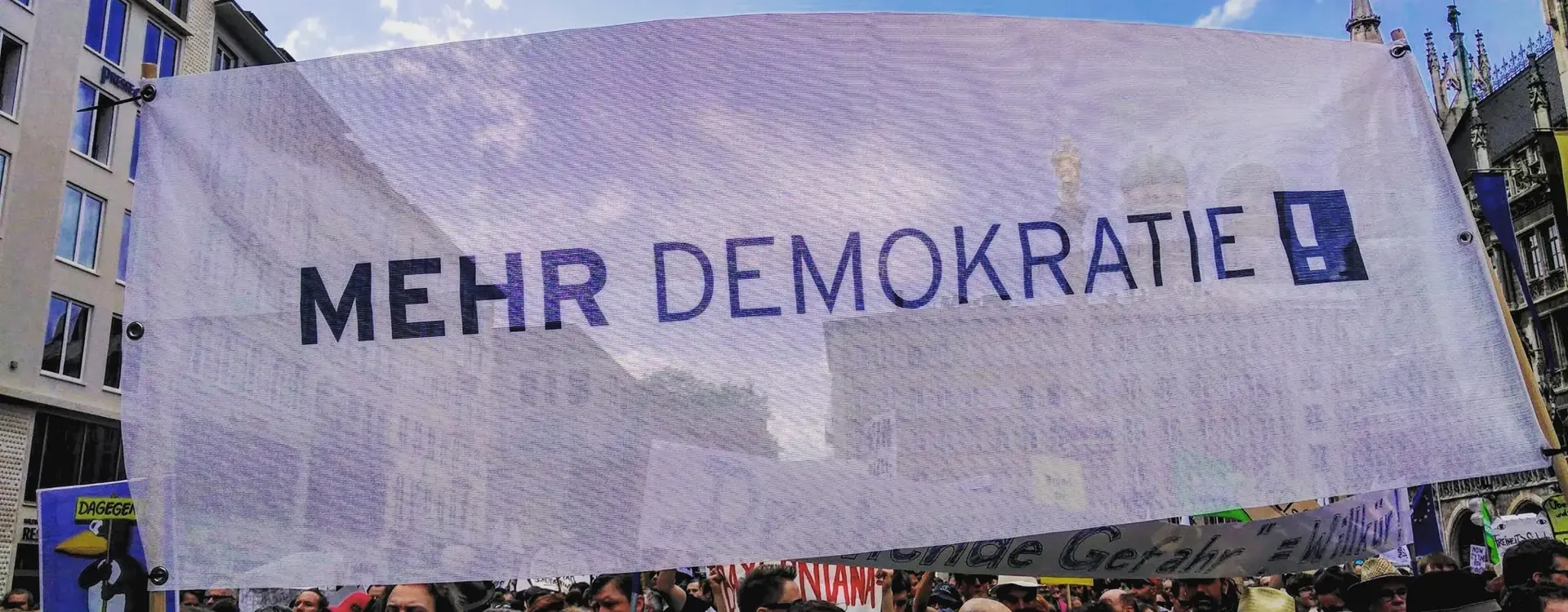 Ein Protestmarsch mit einem Transparent mit dem Logo von Mehr Demokratie ist zu sehen.