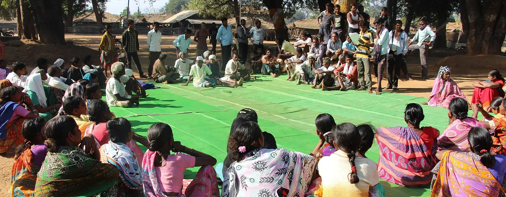 Bewohnerinnen und Bewohner des indischen Dorfes Mendha Lekha sitzen im Freien unter Bäumen zu einer Gram Sabha zusammen. In der Dorfversammlung beraten die Bürgerinnen und Bürger gemeinschaftlich über Angelegenheiten ihres Dorfes