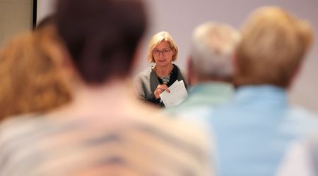 Die saarländische Ministerpräsidentin Anke Rehlinger spricht bei einem Bürgerdialog zum Strukturwandel im Landkreis Merzig-Wadern mit einem Mikrofon zu den Teilnehmerinnen und Teilnehmern. Im Vordergrund sind mehrere Zuhörerinnen und Zuhörer von hinten und unscharf zu sehen; der Blick wird dadurch auf die Rednerin in der Bildmitte gelenkt.