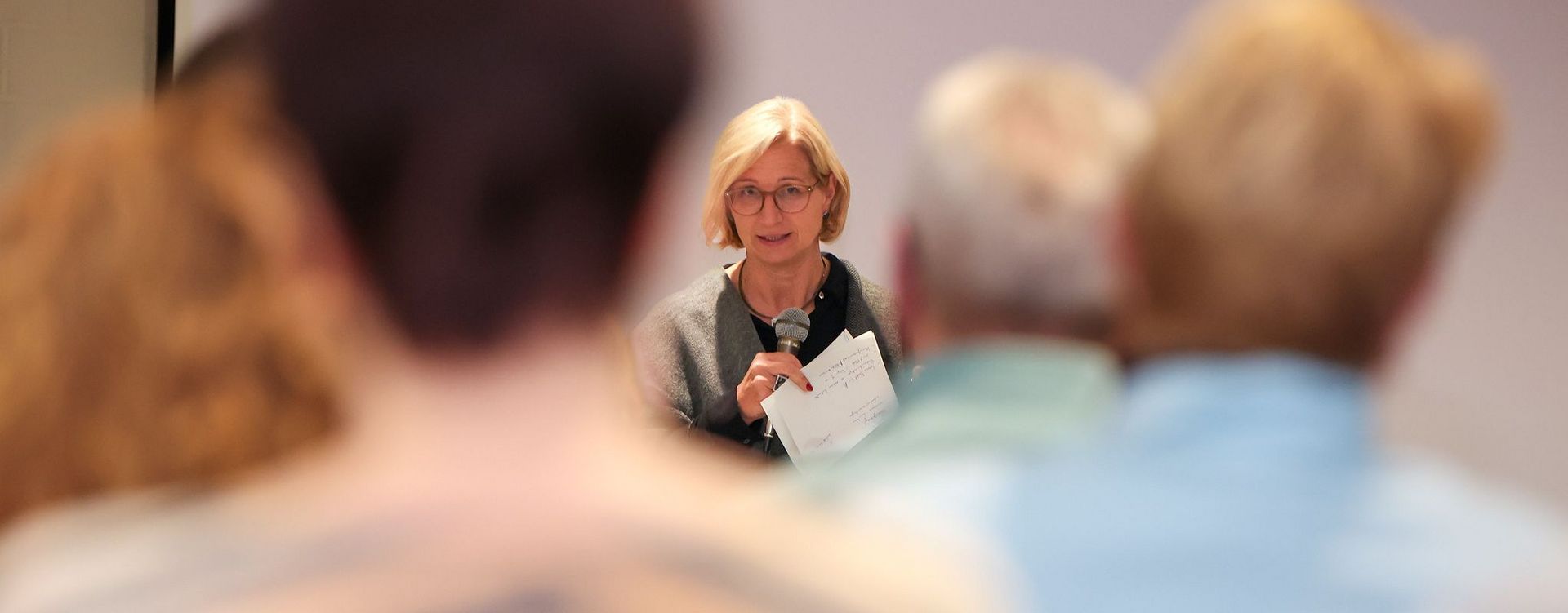 Die saarländische Ministerpräsidentin Anke Rehlinger spricht bei einem Bürgerdialog zum Strukturwandel im Landkreis Merzig-Wadern mit einem Mikrofon zu den Teilnehmerinnen und Teilnehmern. Im Vordergrund sind mehrere Zuhörerinnen und Zuhörer von hinten und unscharf zu sehen; der Blick wird dadurch auf die Rednerin in der Bildmitte gelenkt.