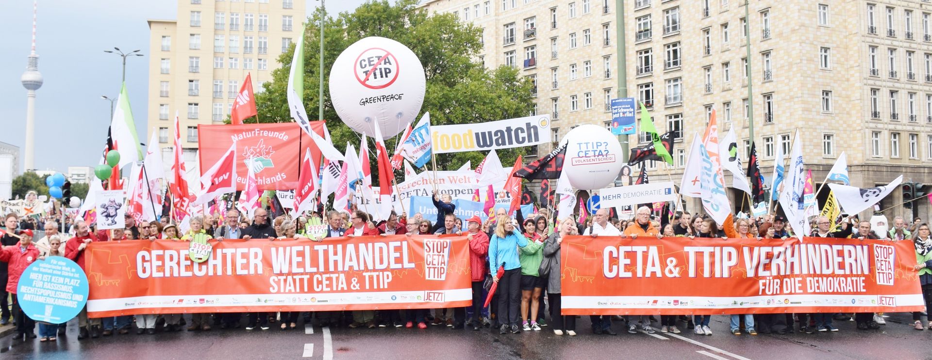 Ein großer Protestmarsch mit roten Bannern und der Aufschrift "Gerechter Welthandel statt CETA & TTIP", ist zu sehen.